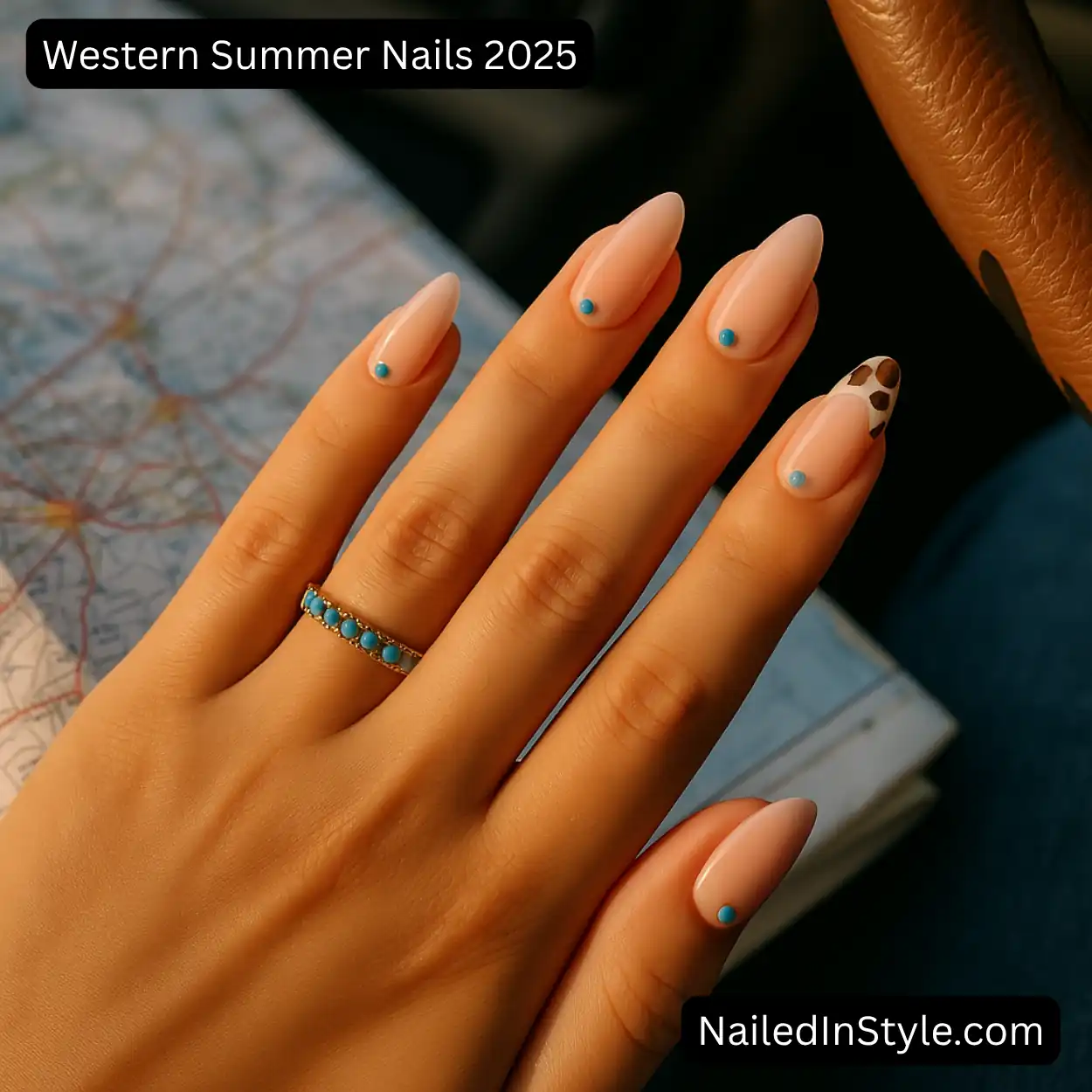 Close-up of a medium-toned hand with almond gel nails in sheer pink, turquoise stud accents, and a cow-print ring finger, resting on a paper road map inside a car; warm sunlight and steering-wheel detail in background.