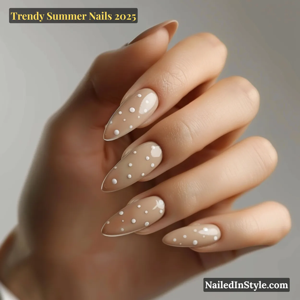 Trendy Summer Nails 2026: Top Designs, Colors & Ideas for the Season 37 Close-up of a fair-toned hand with almond-shaped nails in glossy beige polish and evenly spaced white dot accents.