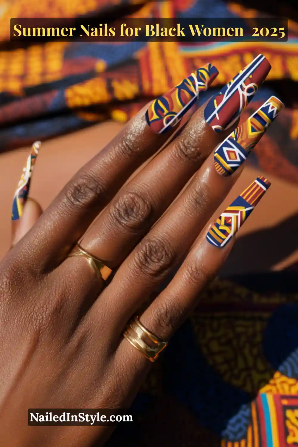 Close-up of a Black woman's hand with long square-shaped nails painted in bold Ankara-inspired tribal prints in red, navy, yellow, and white, against matching African fabric.