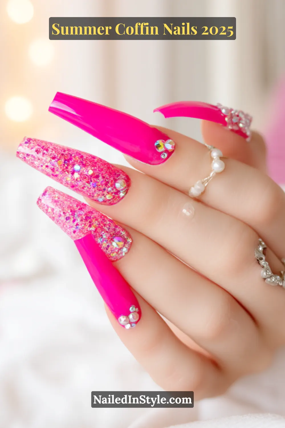 Close-up of long hot pink coffin nails with glitter accents and rhinestone embellishments on a softly lit background