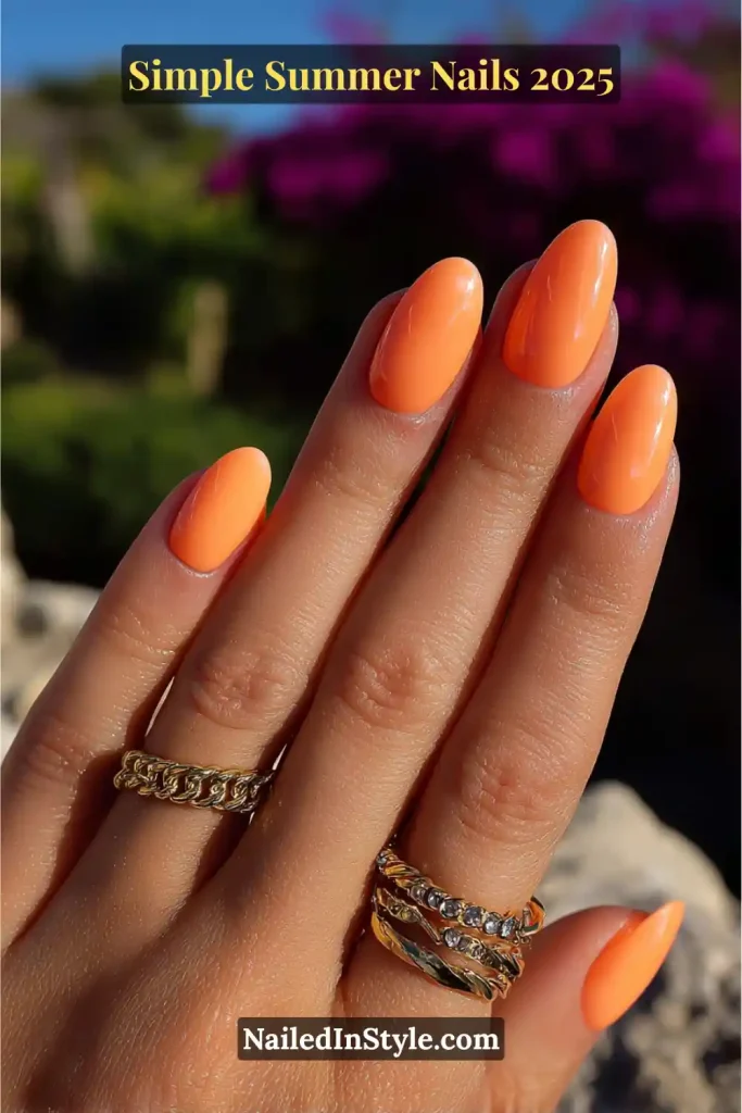Simple Summer Nails Almond-shaped nails painted in bold neon orange polish, worn on a medium-toned hand with gold rings against a floral summer background.