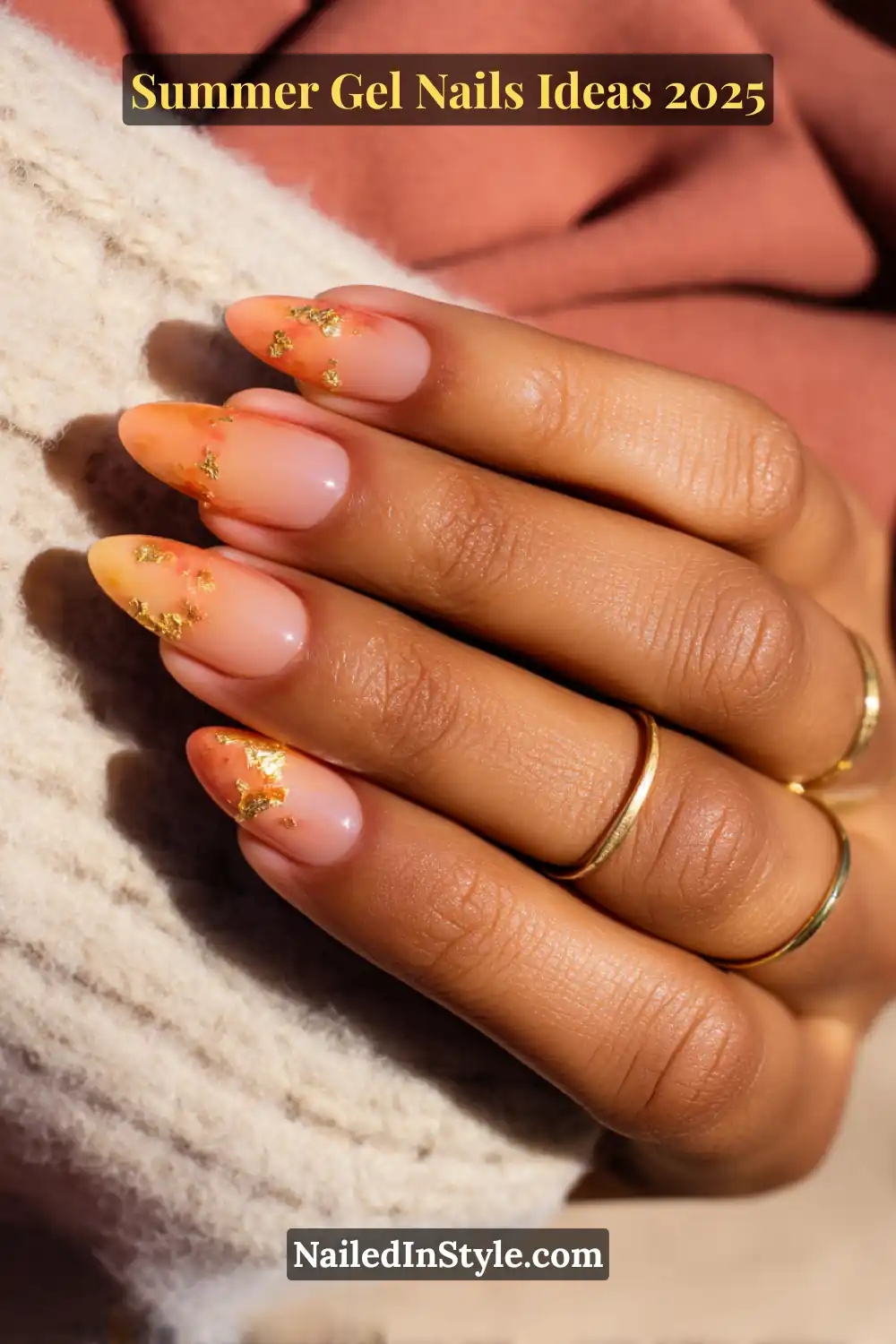 Summer Gel Nails Ideas 2026 2 Close-up of a bronze-toned hand with almond-shaped gel nails featuring a warm ombré gradient from peach to coral orange, detailed with scattered gold foil flakes. Background includes soft beige knit and terracotta tones.