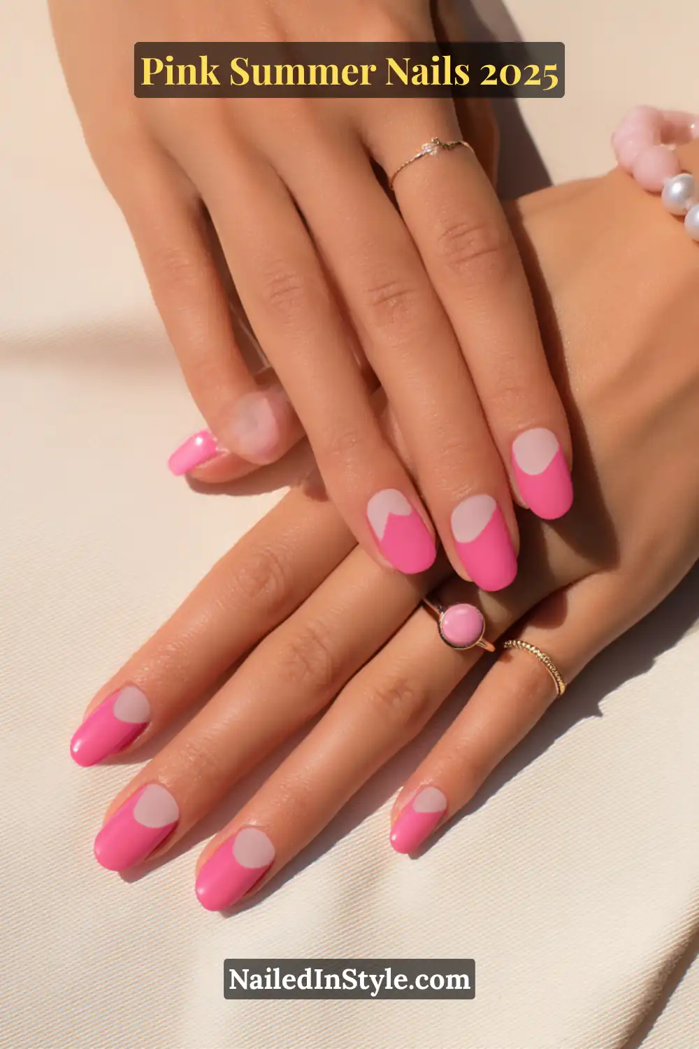 Hands with bubblegum pink nails featuring a minimalist half-moon nude base, complemented by gold and pink jewelry.