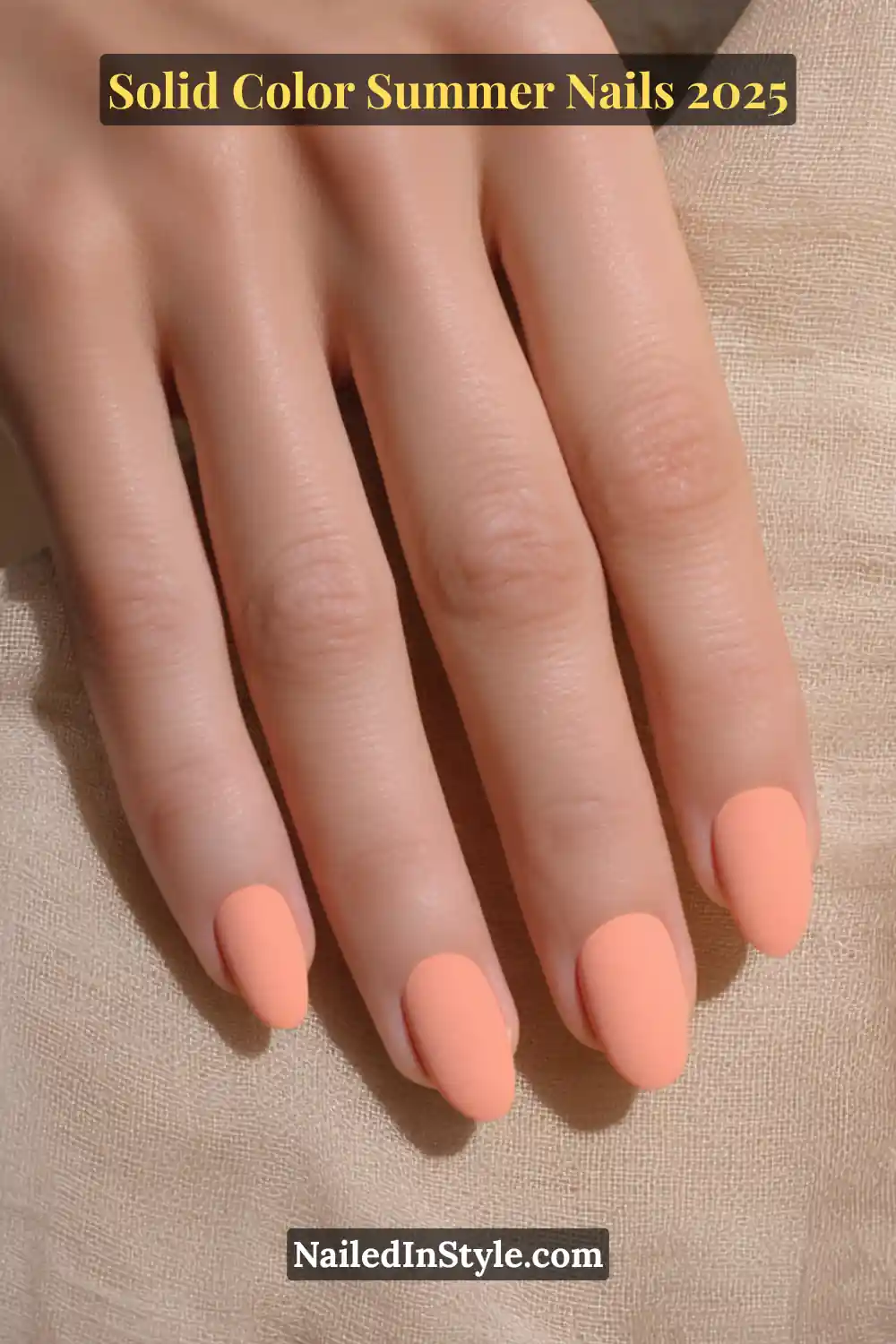 A single hand with almond-shaped nails painted in a soft matte cantaloupe orange shade, resting on a textured beige fabric.
