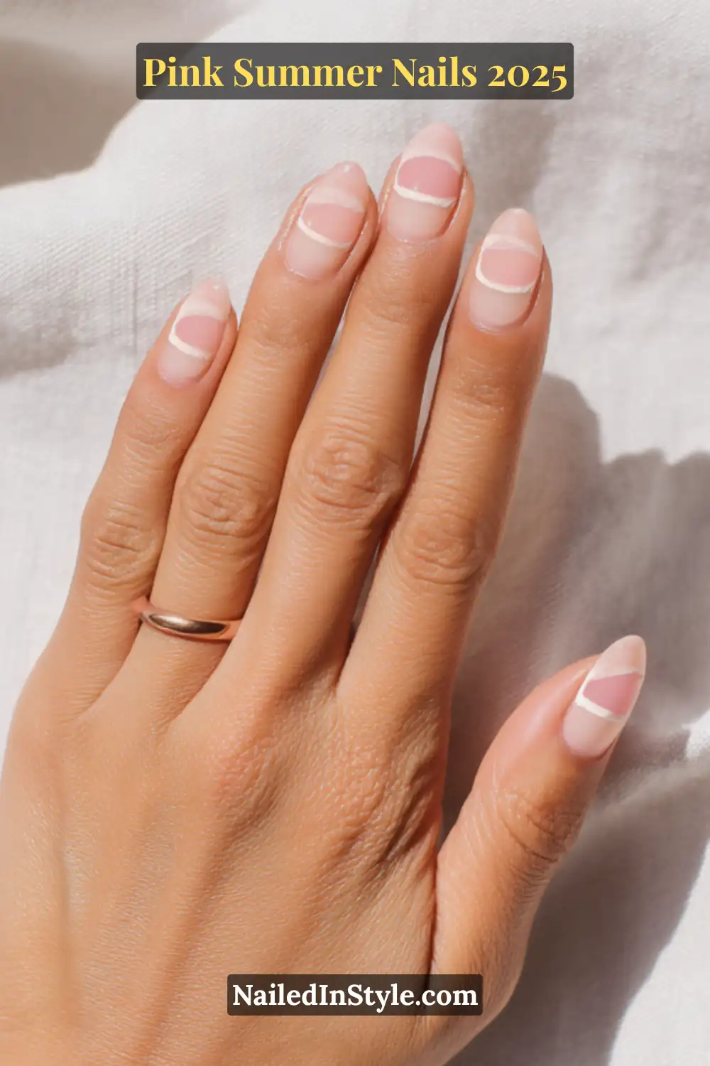Close-up of a hand with almond-shaped nails featuring translucent nude polish and clean pink linear accents using negative space, styled with a pink wrap bracelet and gold ring.