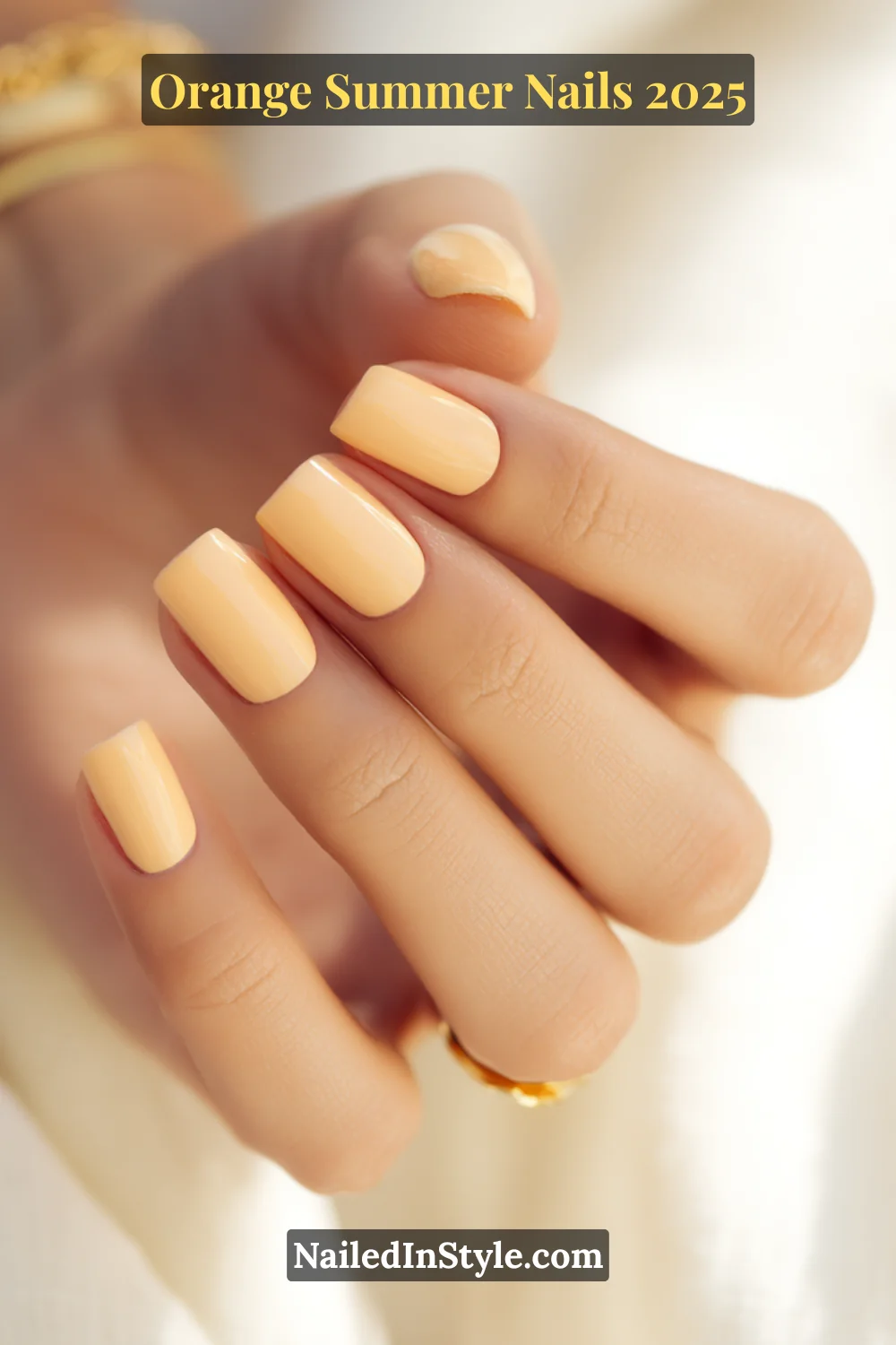 Close-up of a hand with glossy, soft tangerine square-shaped nails in a creamy orange hue, styled against a warm, sunlit background.