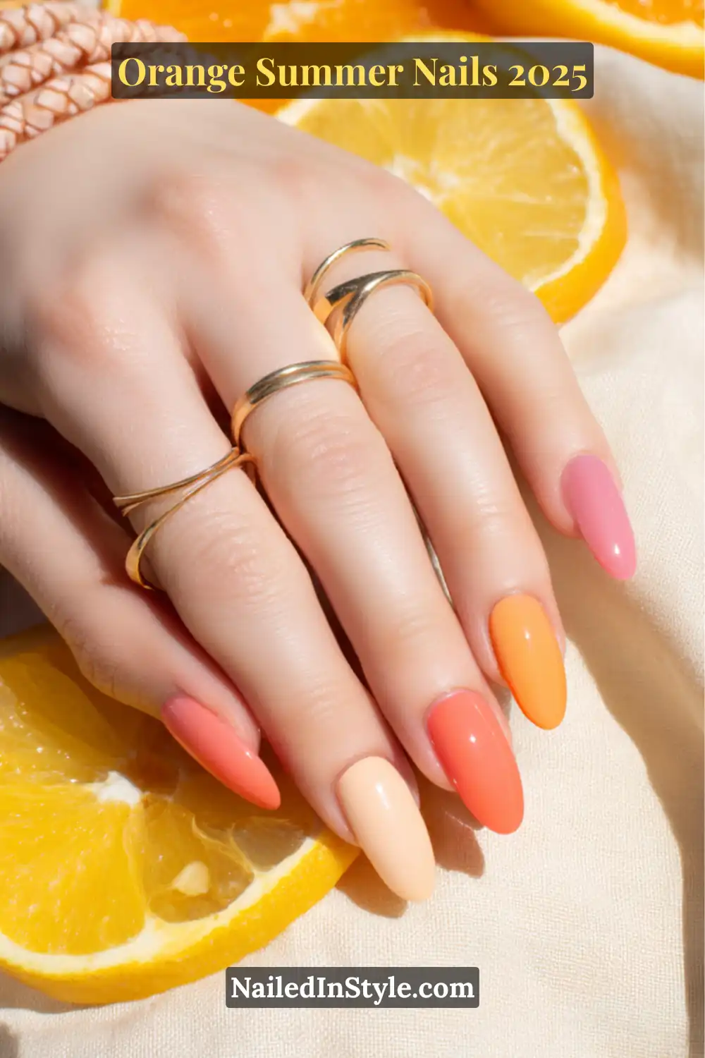Hand with fair skin showcasing gradient orange-toned nails in peach, coral, and tangerine shades, accessorized with gold rings and fresh orange slices.