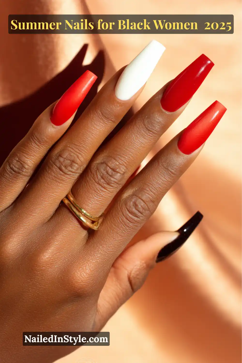 Close-up of a Black woman's hand with long coffin nails painted in bold red, white, nude, and black shades for a classic summer baddie look.