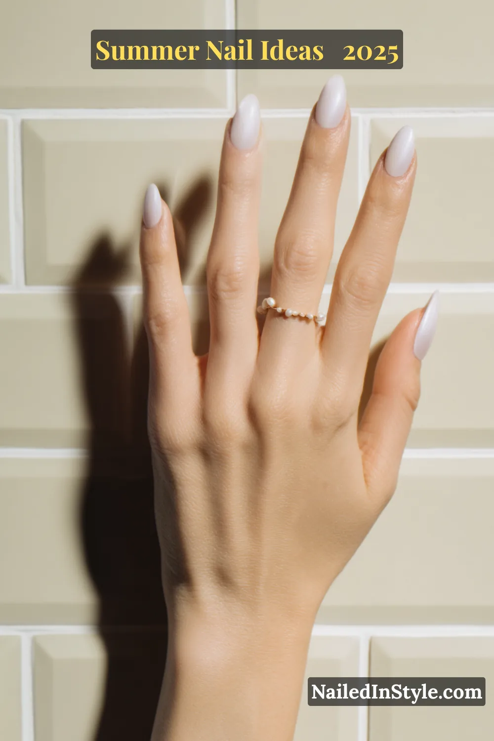 Single hand with almond-shaped vanilla chrome nails featuring a subtle blush glow effect, held against glossy beige tile.