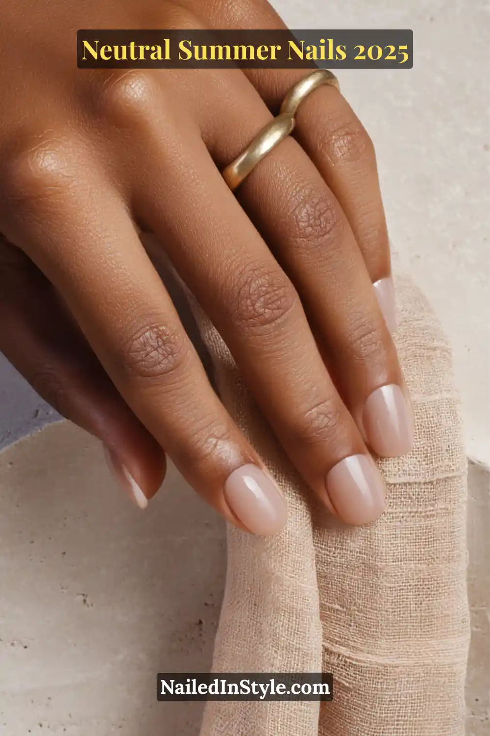 Neutral Summer Nails 2026: Clean, Chic & Warm-Weather Ready 9 Close-up of hand with clean, short, rounded nails painted in a clear nude gel polish, styled with a bold matte gold ring and neutral linen textures.