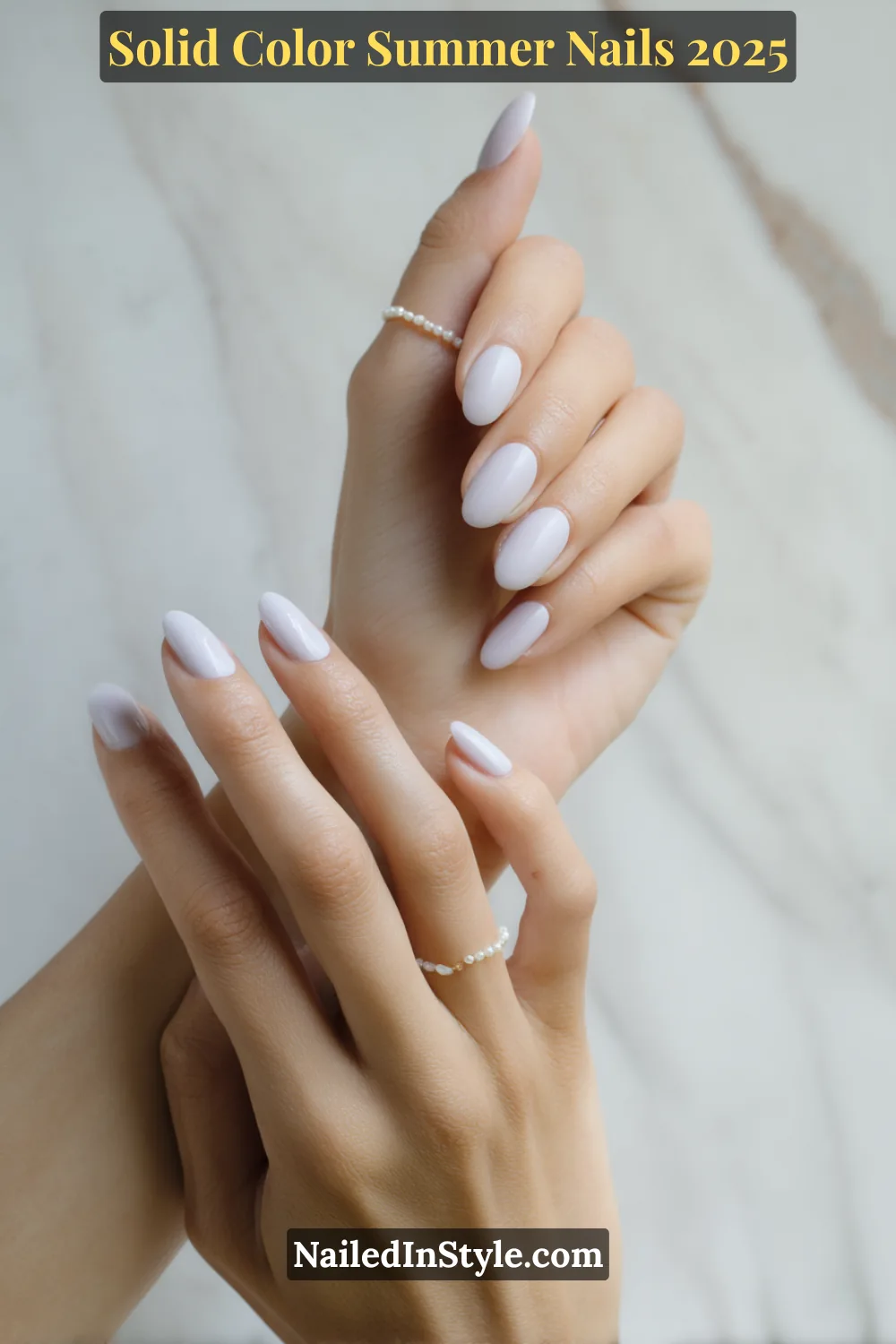 Two hands with almond-shaped nails painted in a soft, pastel cloudy lilac cream polish with a glossy finish, styled with minimal pearl rings.