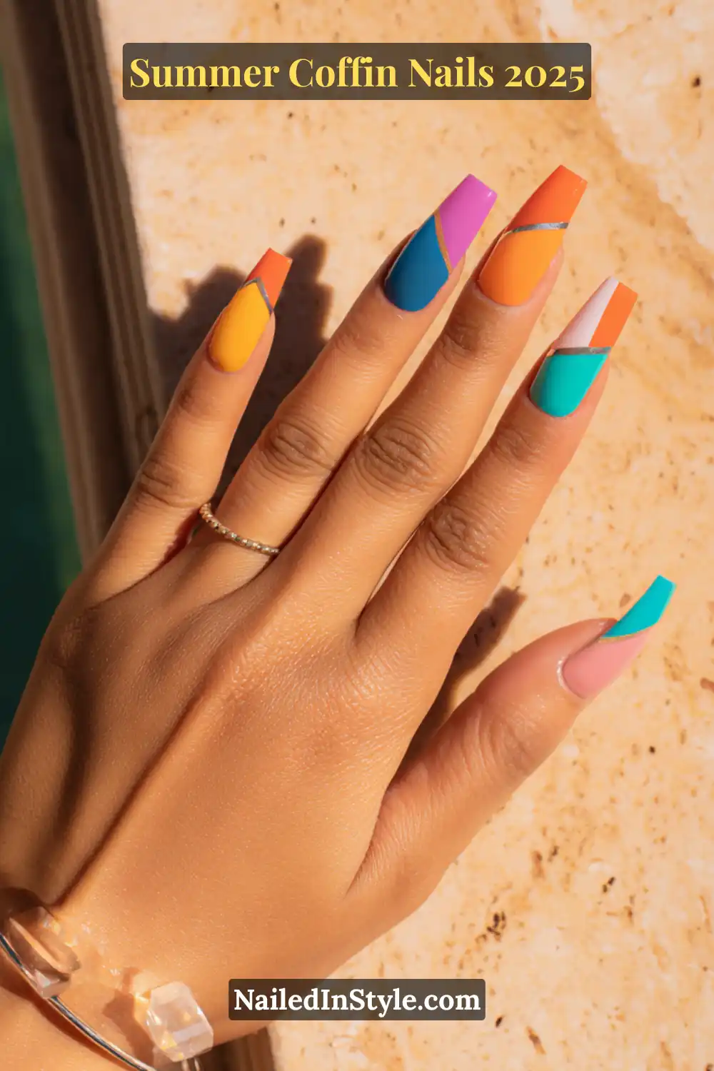Hand with long coffin nails painted in vibrant color block sections including orange, teal, cobalt, and pink, designed for summer nail trends.