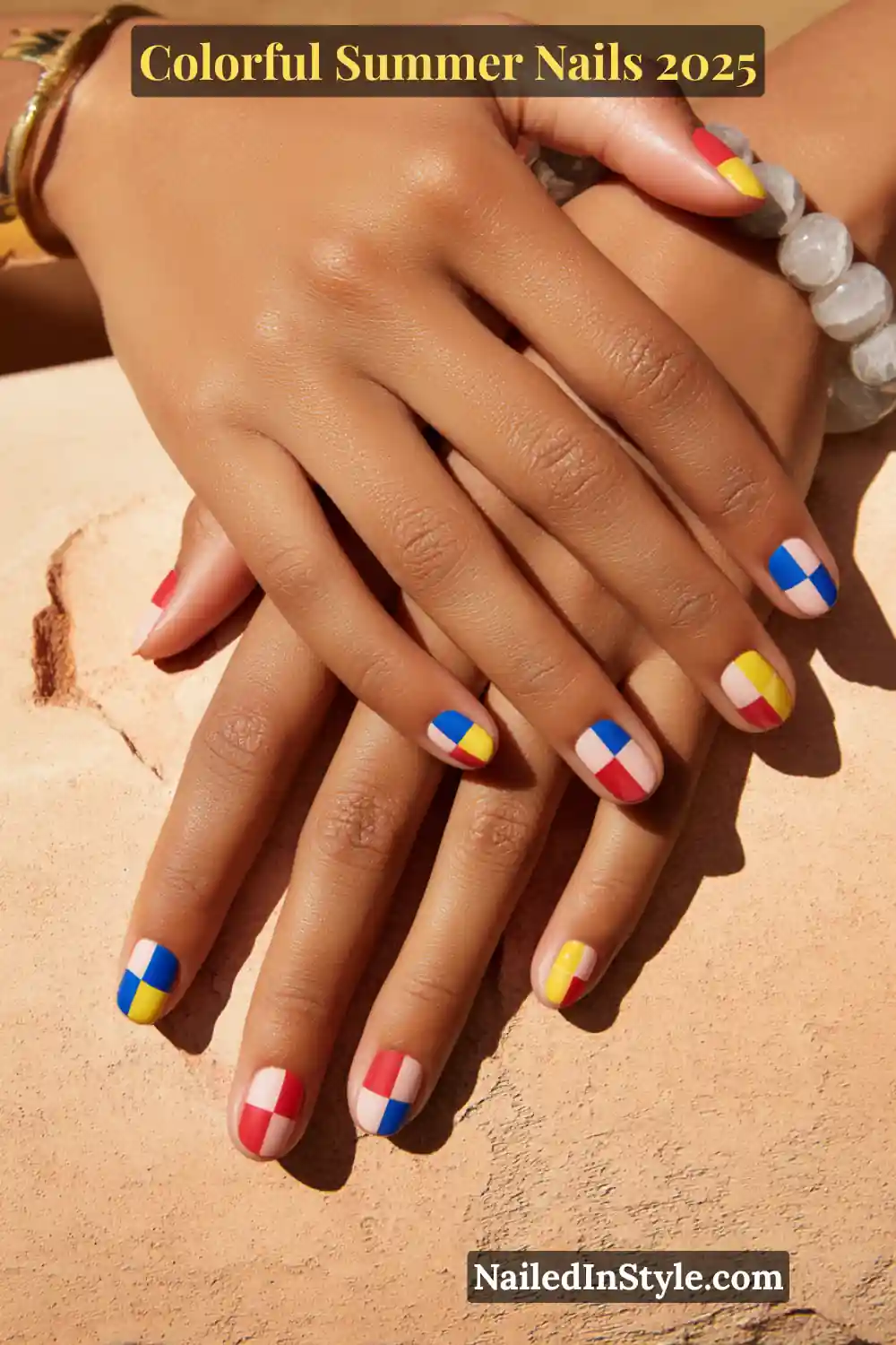 Colorful Summer Nails 2026: Bold, Fun & Bright Manicure Ideas 16 Two hands with medium tan skin tone featuring short square nails with checkerboard designs in red, yellow, blue, and pink over a nude base