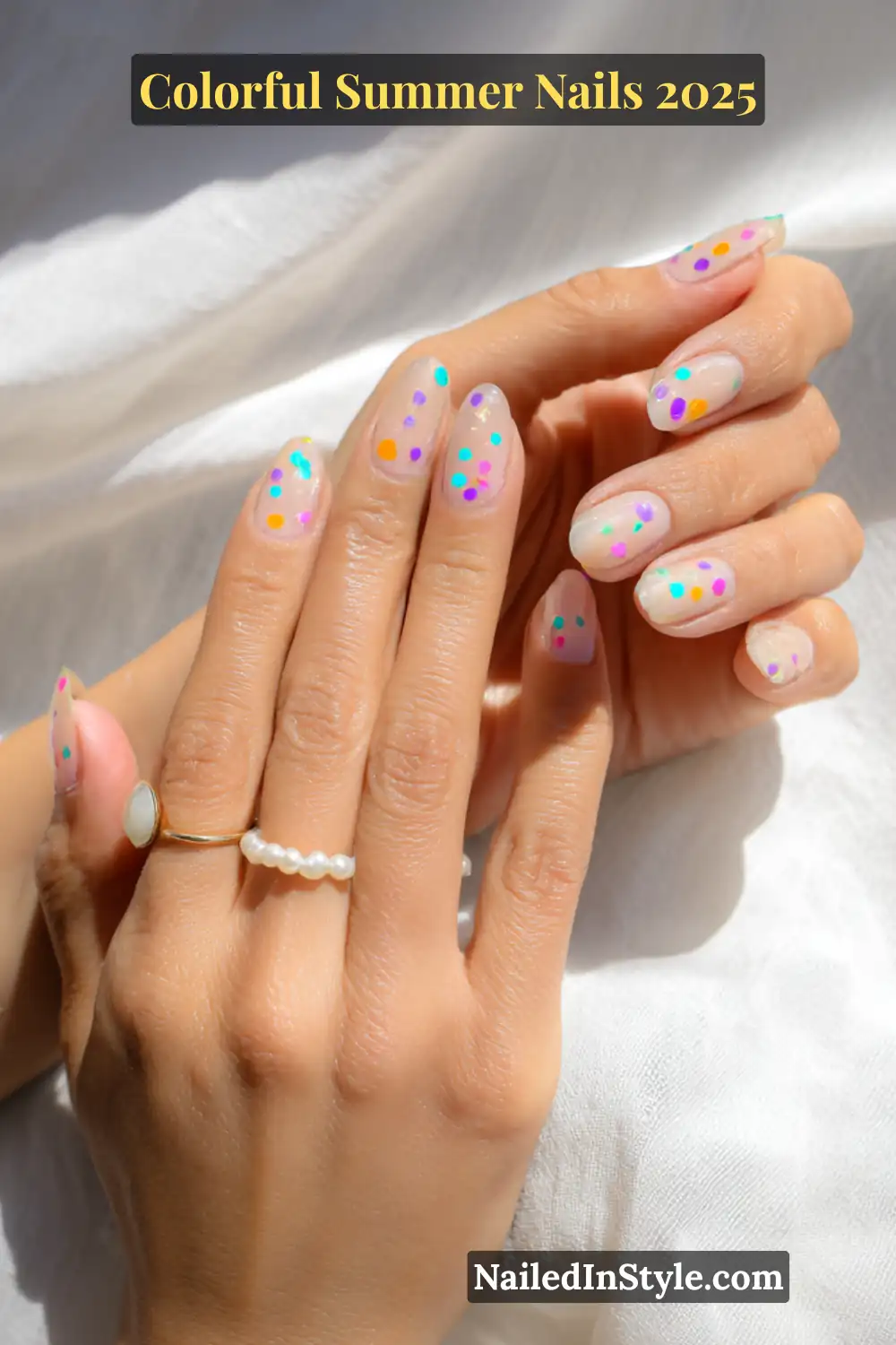 Colorful Summer Nails 2026: Bold, Fun & Bright Manicure Ideas 22 Hands with light skin tone featuring almond-shaped nails painted with multicolored confetti dots over a translucent white base, glowing in natural sunlight