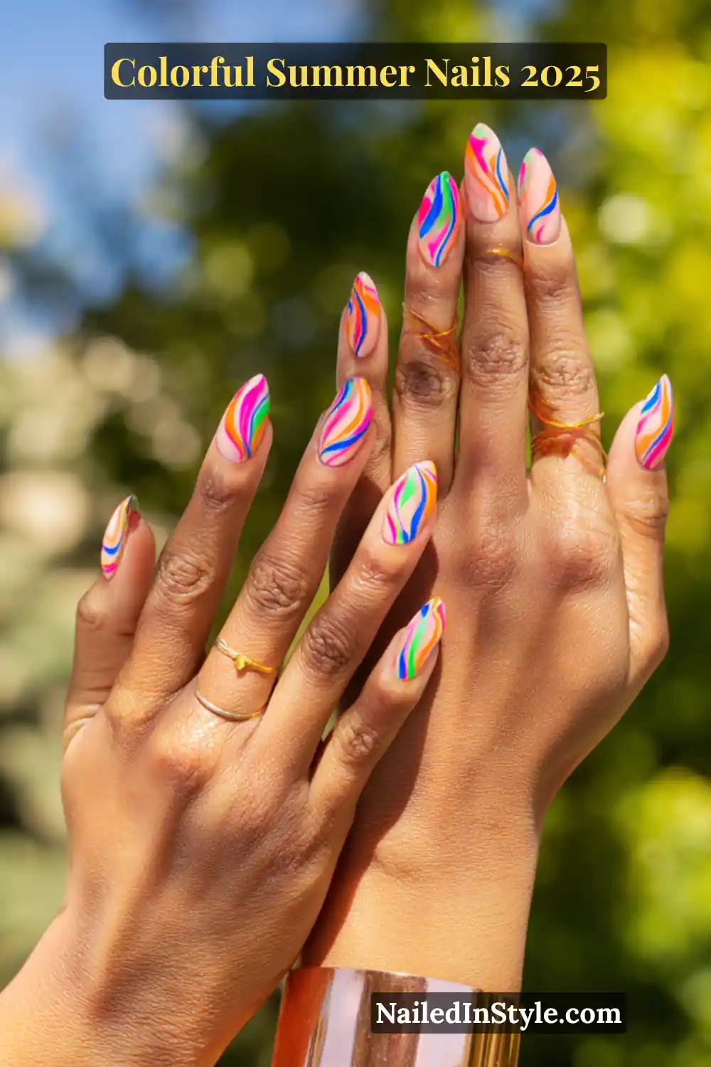 Colorful Summer Nails 2026: Bold, Fun & Bright Manicure Ideas 20 Two hands with medium-deep skin tone featuring almond-shaped nails with multicolor swirl designs in hot pink, orange, lime green, blue, and purple on a nude base