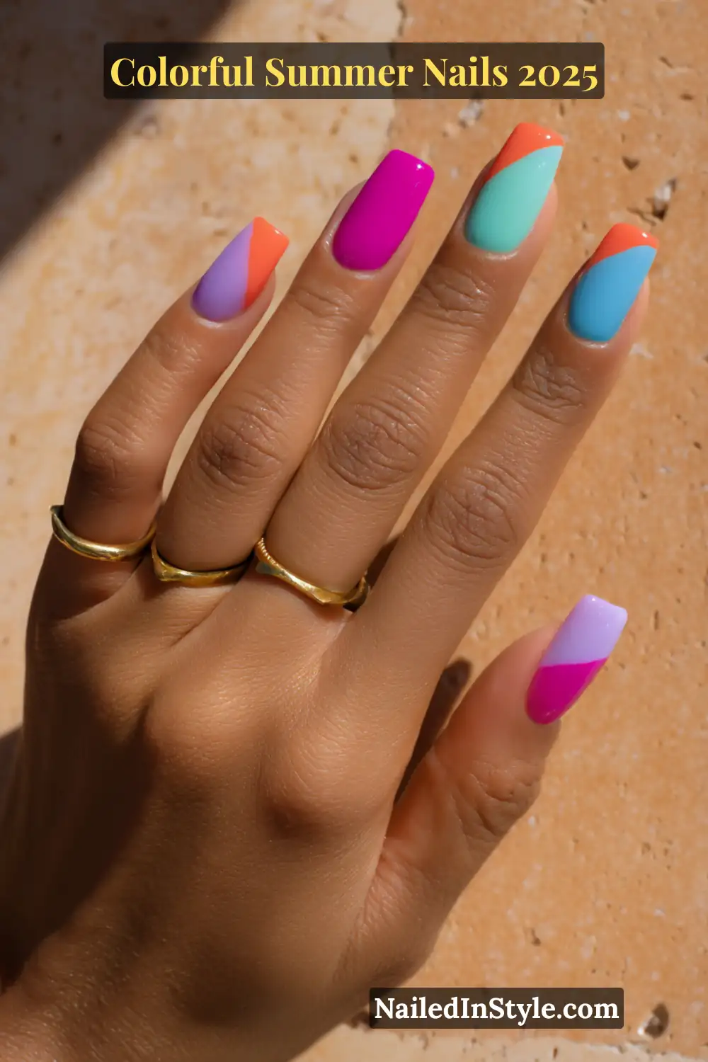 Colorful Summer Nails 2026: Bold, Fun & Bright Manicure Ideas 15 Hand with medium tan skin tone showing square nails with diagonal color block designs in bold shades like lavender, orange, hot pink, teal, and sky blue