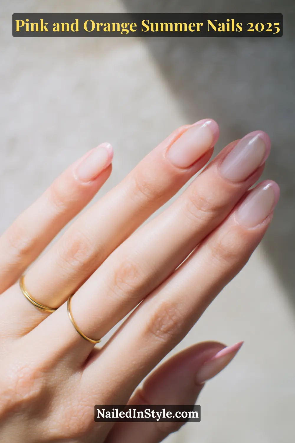 Pink and Orange Summer Nails 2026: Sunset Tips, Endless Vibes 16 Hand with almond-shaped nails in a sheer coral base and soft baby pink tips, shown in a resting pose on fair skin with gold rings.
