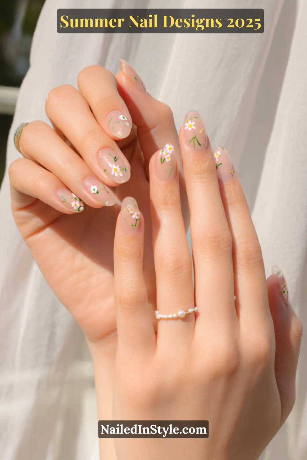 Hands with almond-shaped nails featuring tiny white daisy flower nail art on a translucent pinky-beige base