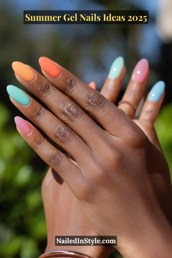Summer Gel Nails Ideas Close-up of a deep cocoa-toned hand with almond-shaped gel nails in a rainbow palette: mint green, peach orange, tangerine, cotton candy pink, and baby blue, all with a glossy summer finish. Background includes soft-focus greenery under daylight.