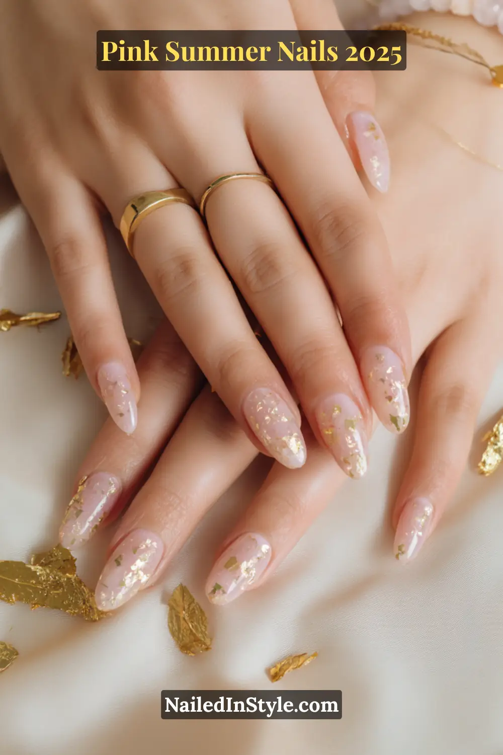 Close-up of feminine hands featuring almond-shaped glossy pink nails embedded with scattered gold foil accents, surrounded by gold leaf decor.