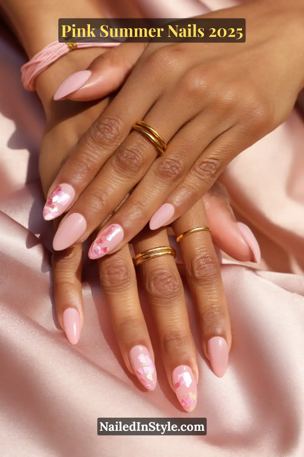Hands with almond-shaped pastel pink nails featuring one-nail foil art accents on a silky pink background.