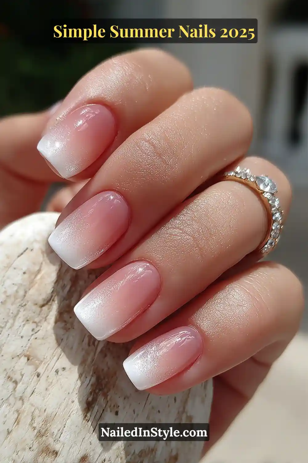 Natural fair-toned hand with short square nails in a soft white ombré gradient, glossy finish, and diamond ring in sunlight.
