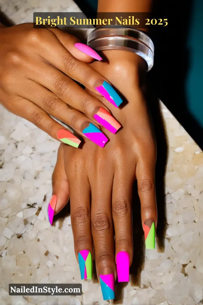 Close-up of hands with long square nails painted in neon pink, green, blue, and orange geometric shapes on a natural base.