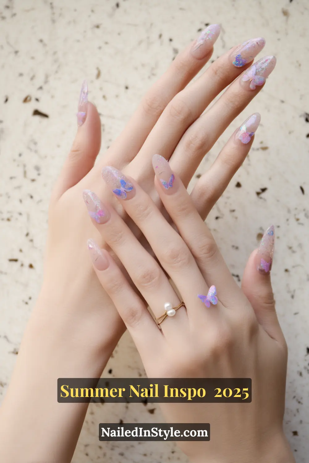 Close-up of hands with almond-shaped nails featuring translucent pink polish, iridescent glitter, and 3D butterfly decals in blue and lavender.