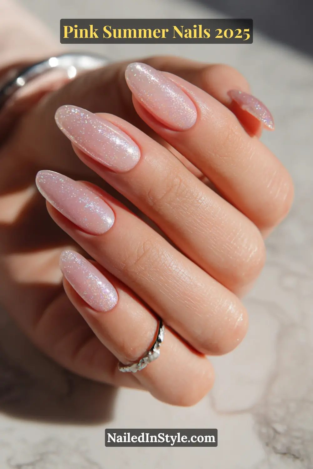 Close-up of hand with almond-shaped nails painted in a translucent pink shimmer polish over a clear base, ideal for summer 2025.