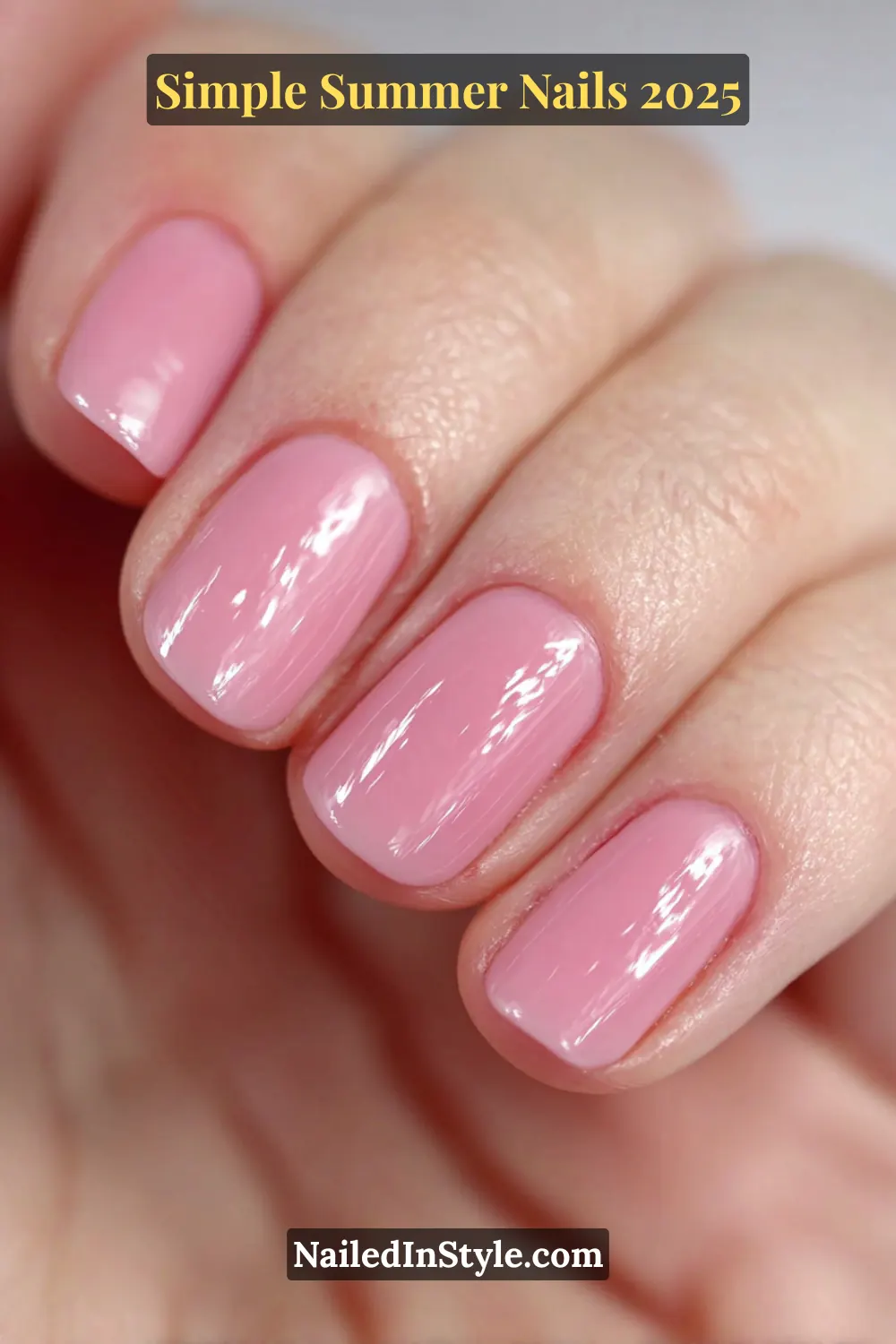 Close-up of short square nails painted in a shiny bubblegum pink polish on a fair-skinned hand.