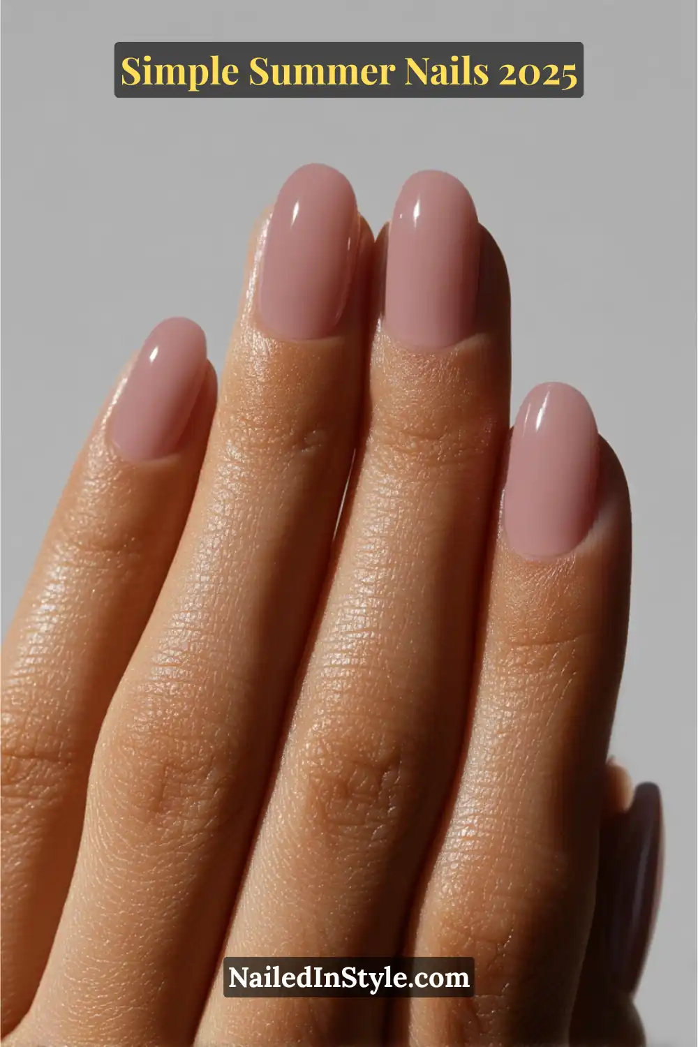 A hand with golden-tan skin tone displays medium-length oval nails painted in a glossy mauve nude polish, photographed in soft natural light against a minimalist background.