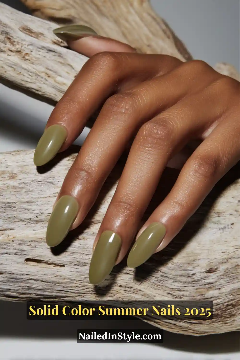 Hand with almond-shaped glossy olive green nails resting on textured driftwood.