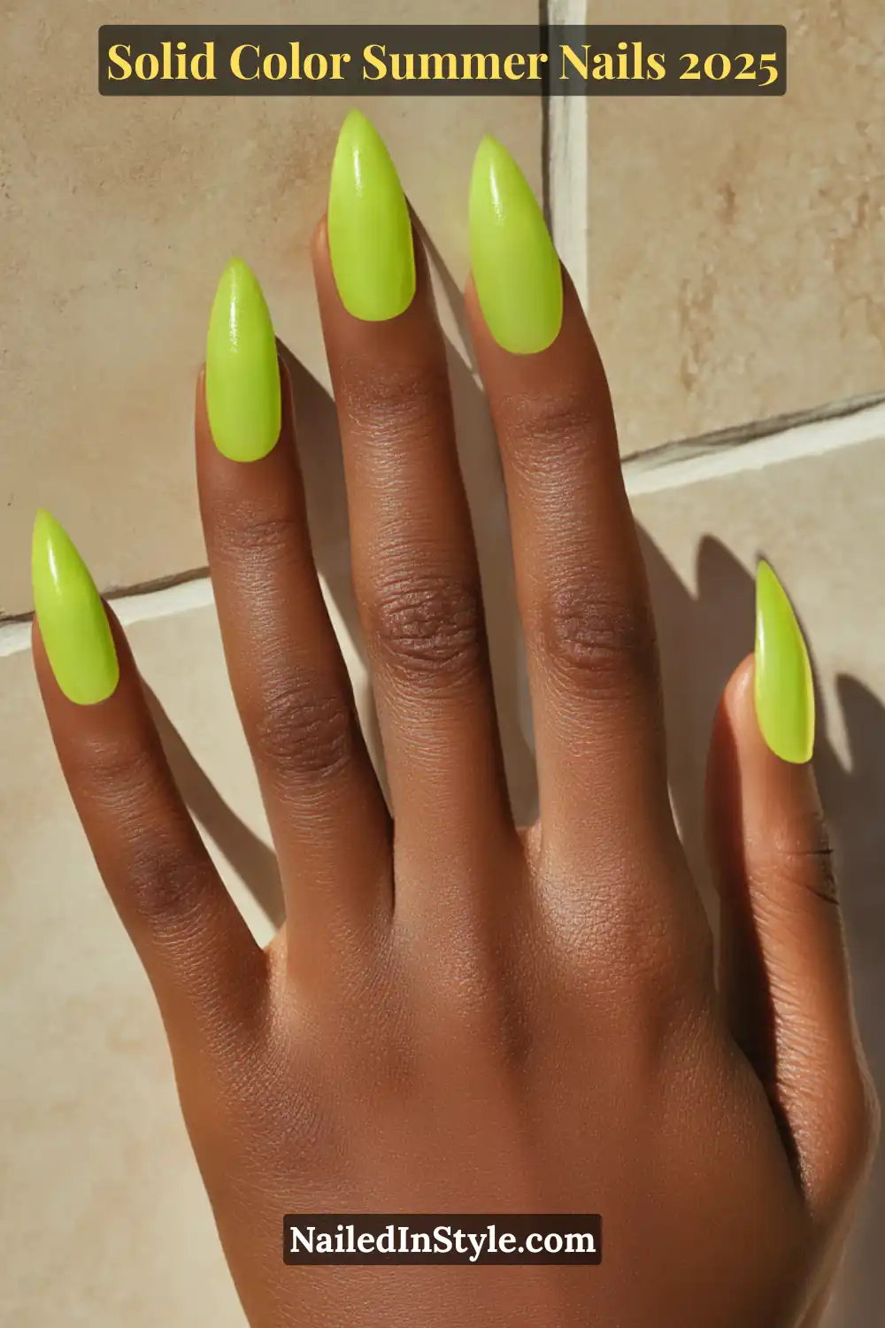 Hand with almond-shaped neon green nails glowing in the sunlight against a neutral tile background.