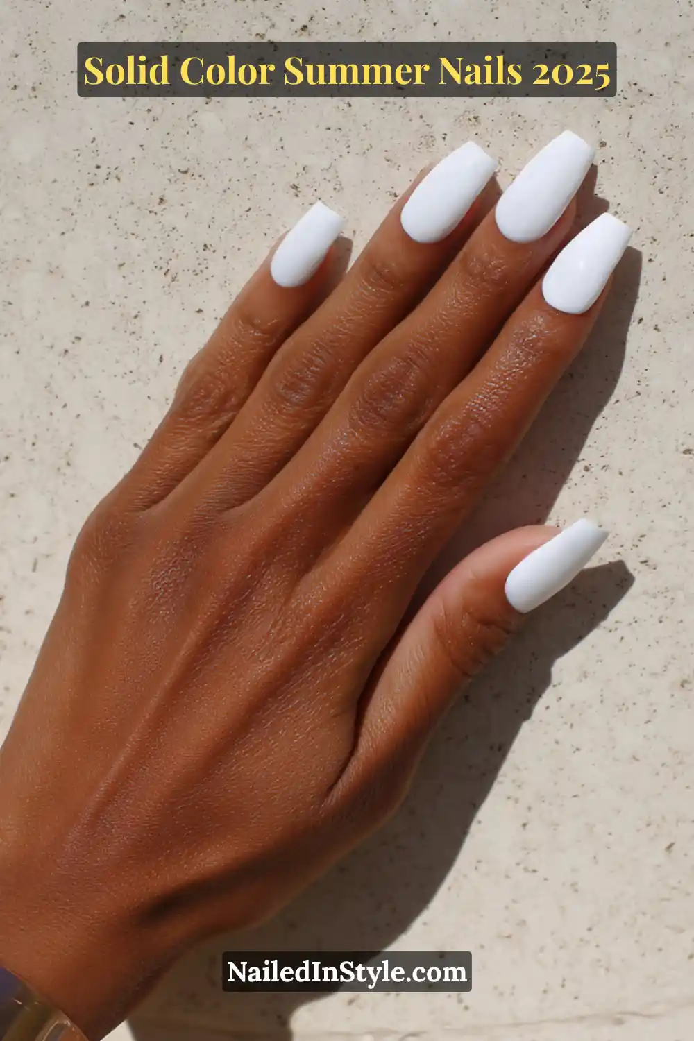 A hand with long square-shaped nails painted in a bright icy white polish, resting on a sunlit stone surface.