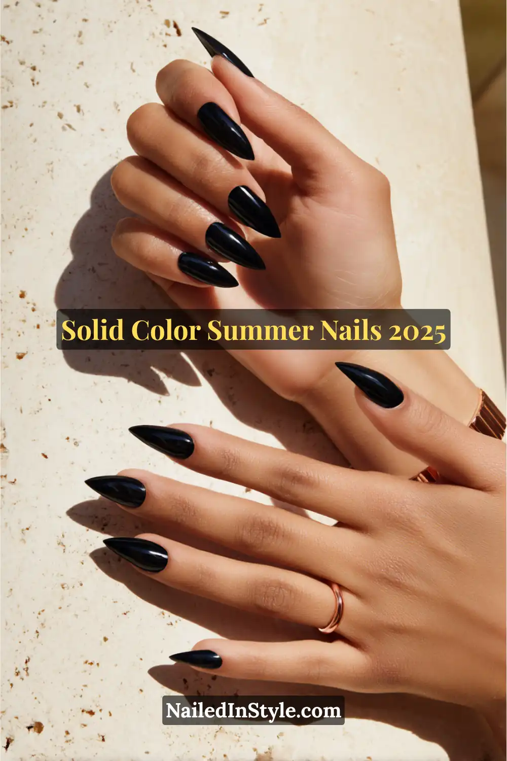 Hands with sharp almond-shaped glossy jet black nails, resting on a sunlit stone surface.