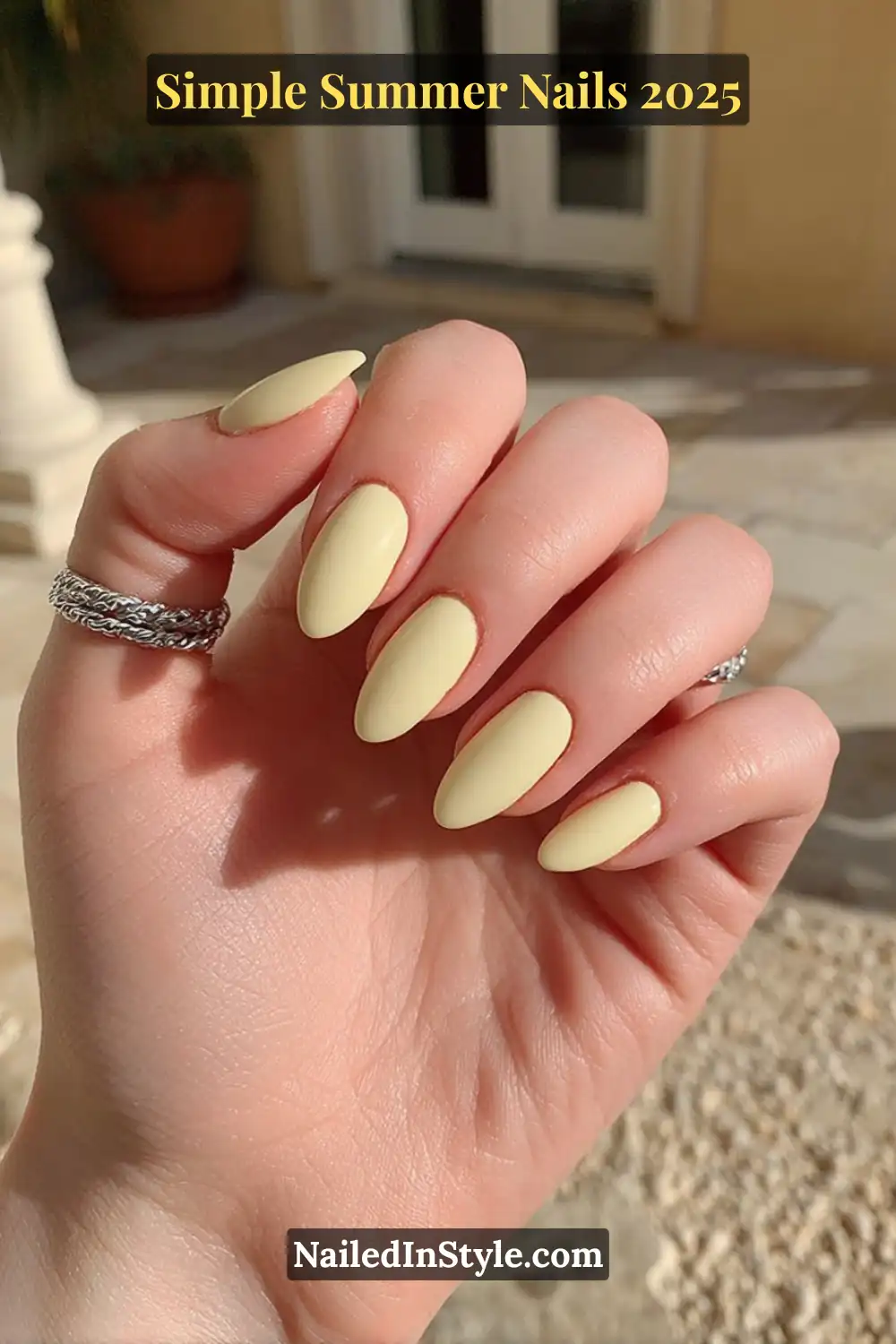 Close-up of a hand with almond-shaped nails painted in a vivid lemon yellow polish, glowing under summer sunlight.