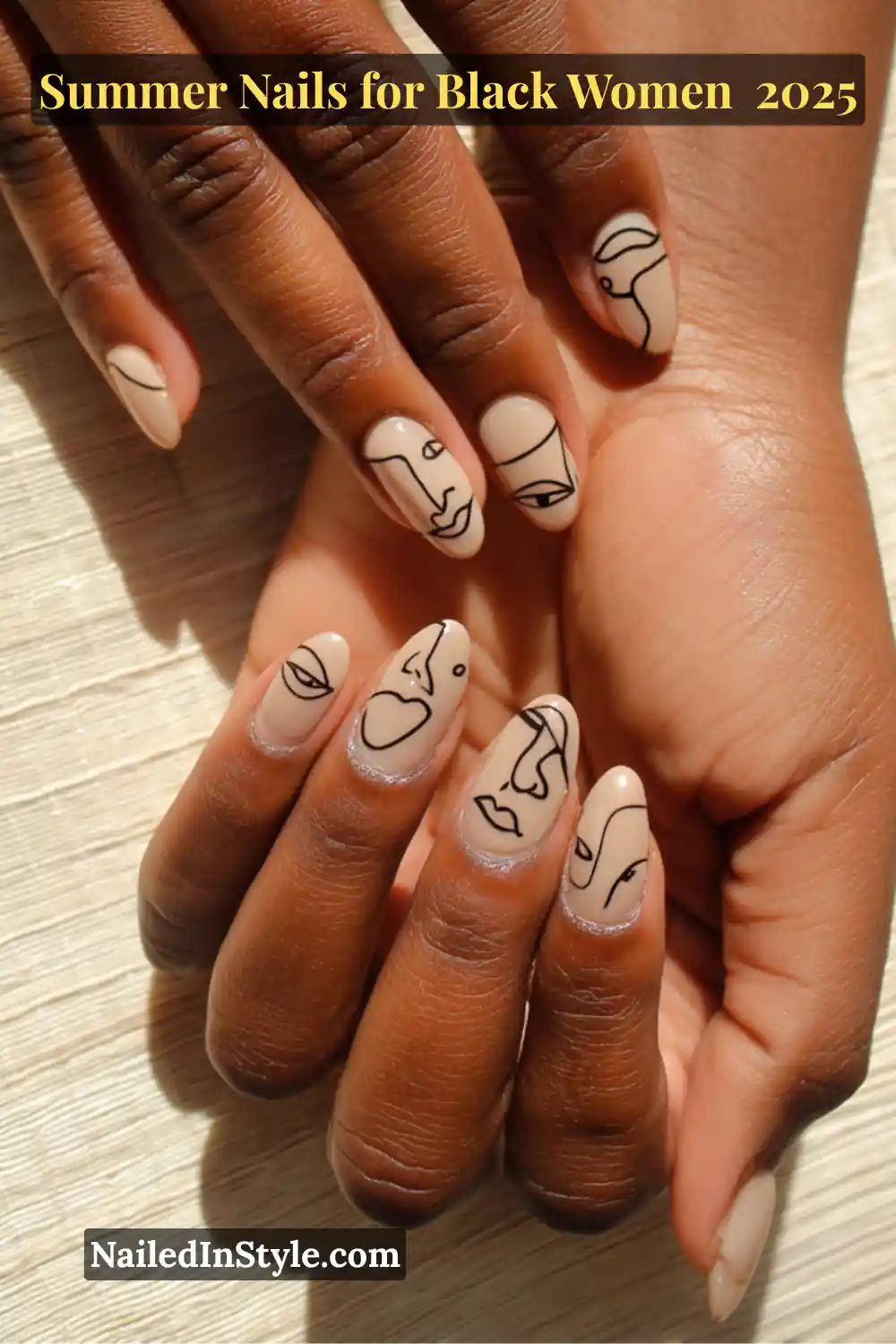 Close-up of Black woman's hands featuring nude almond-shaped nails with hand-painted abstract black line art of faces and eyes, resting on a sunlit wooden surface.