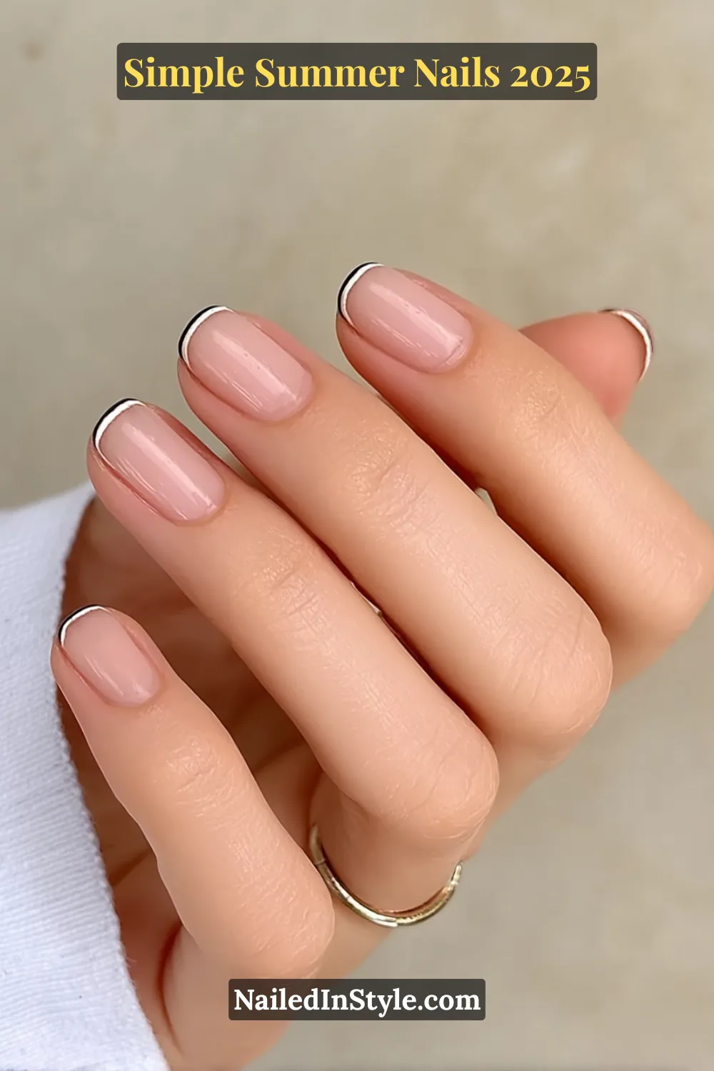 A fair-toned hand with short natural nails painted in a sheer nude base and topped with ultra-thin white and black micro French tips. The look is clean and elegant.