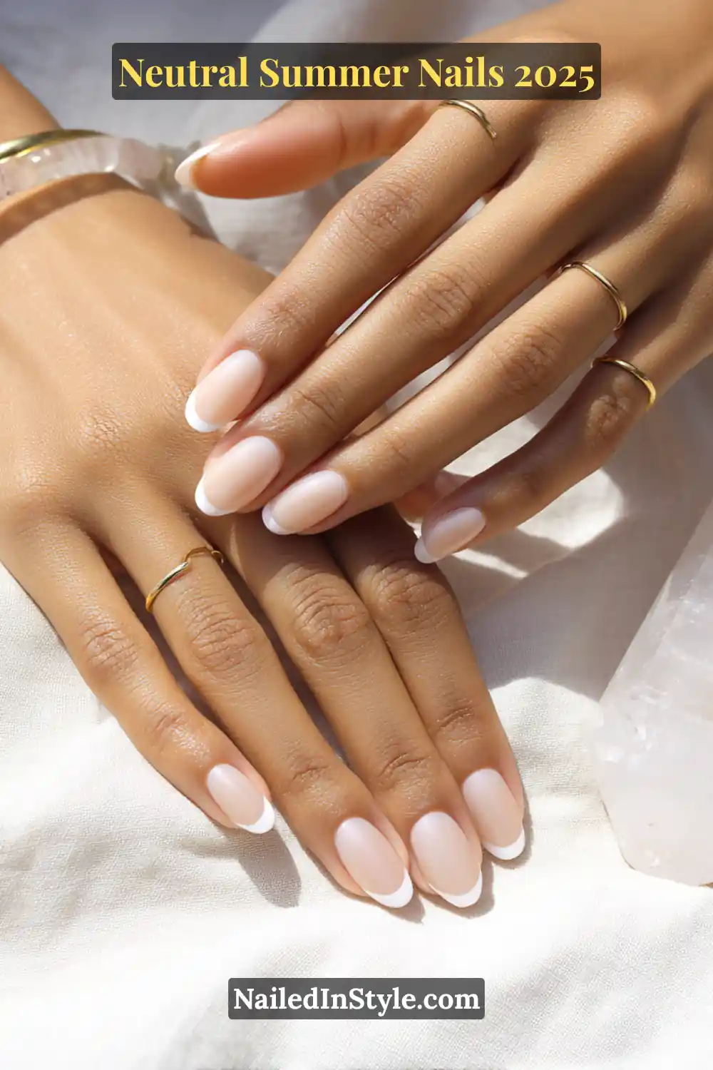 Neutral Summer Nails 2026: Clean, Chic & Warm-Weather Ready 11 Close-up of hands with a nude French manicure featuring clean white tips on soft pink nude nails, styled with minimalist gold rings on warm-toned skin.