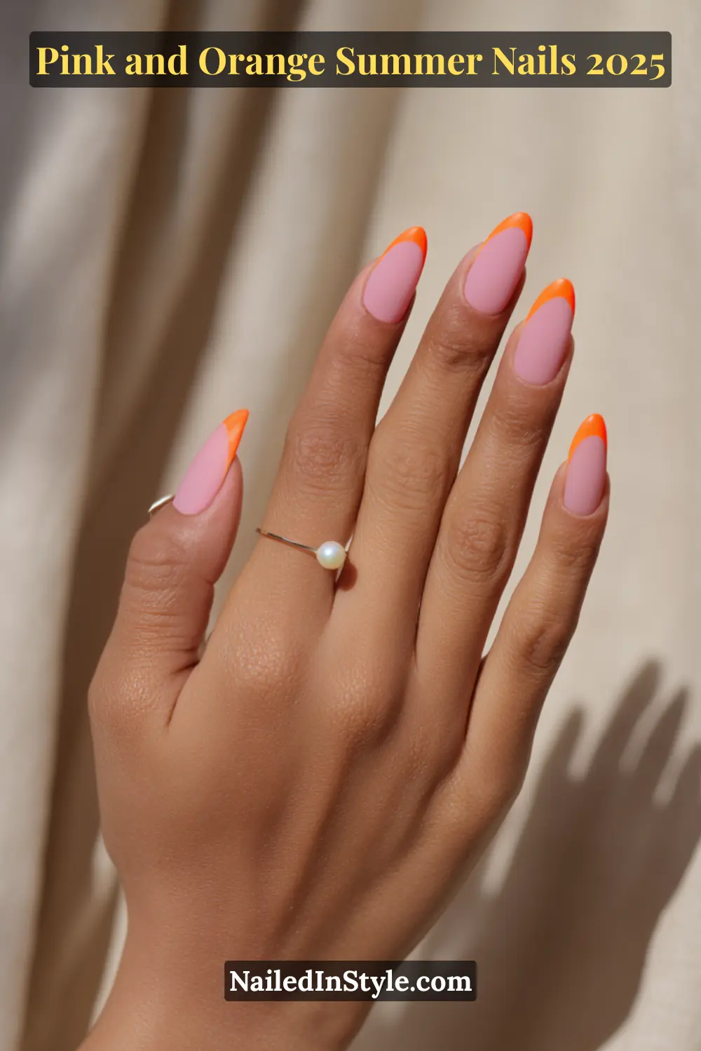Pink and Orange Summer Nails 2026: Sunset Tips, Endless Vibes 14 Hand with almond-shaped matte pink nails and neon orange French tips, posed in soft natural light with pearl and gold rings on tan skin.