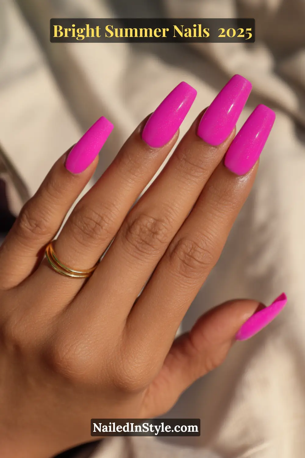 Close-up of a hand with long neon pink coffin nails, glowing under sunlight for a bold summer manicure look.