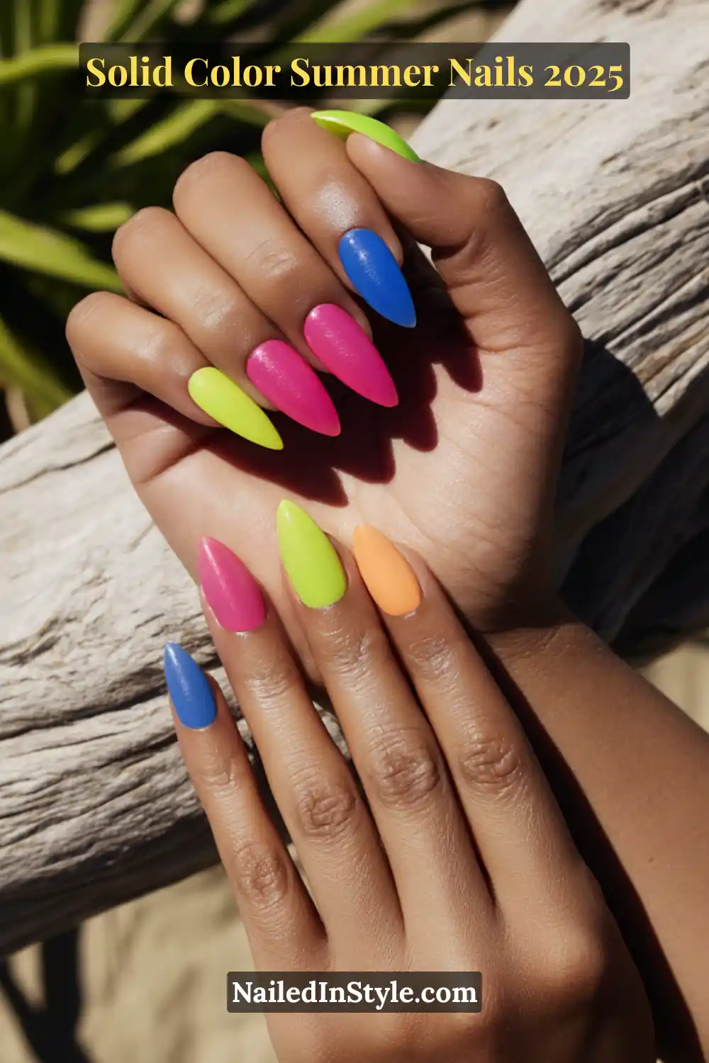 Two hands with long stiletto nails painted in solid neon shades including lime green, cobalt blue, hot pink, and soft orange, displayed outdoors on a sunny day.
