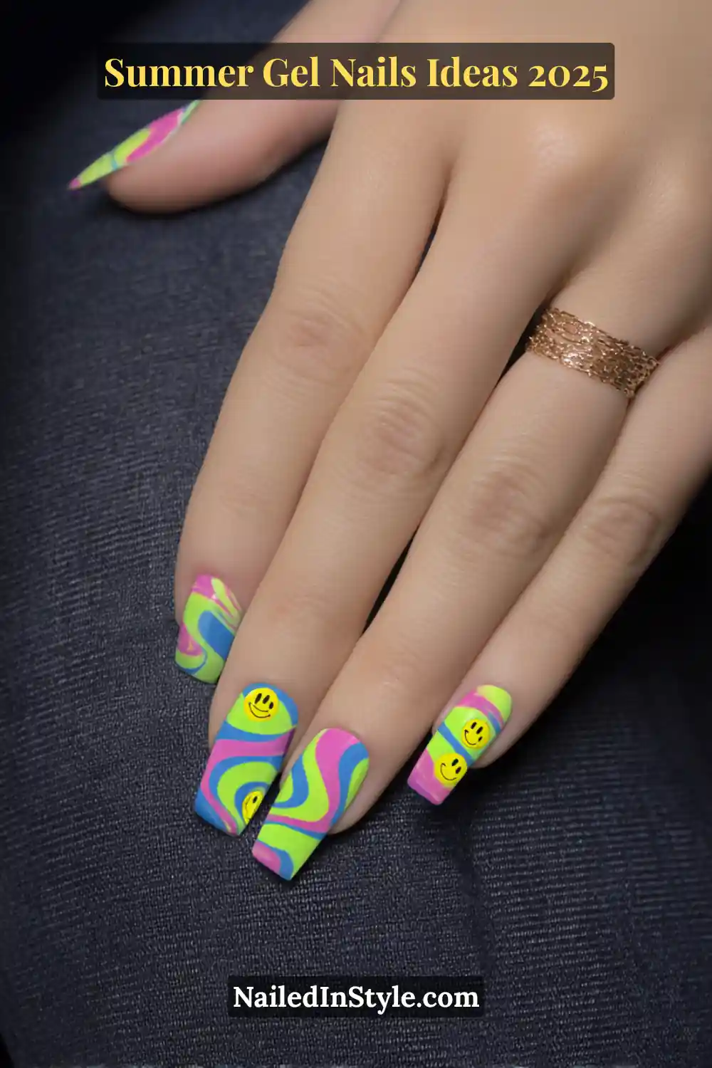 Summer Gel Nails Ideas 2026 4 Close-up of fair-toned hands with square gel nails in neon pink, lime green, blue, and purple swirl patterns, featuring yellow smiley face decals. Background is dark denim for contrast.