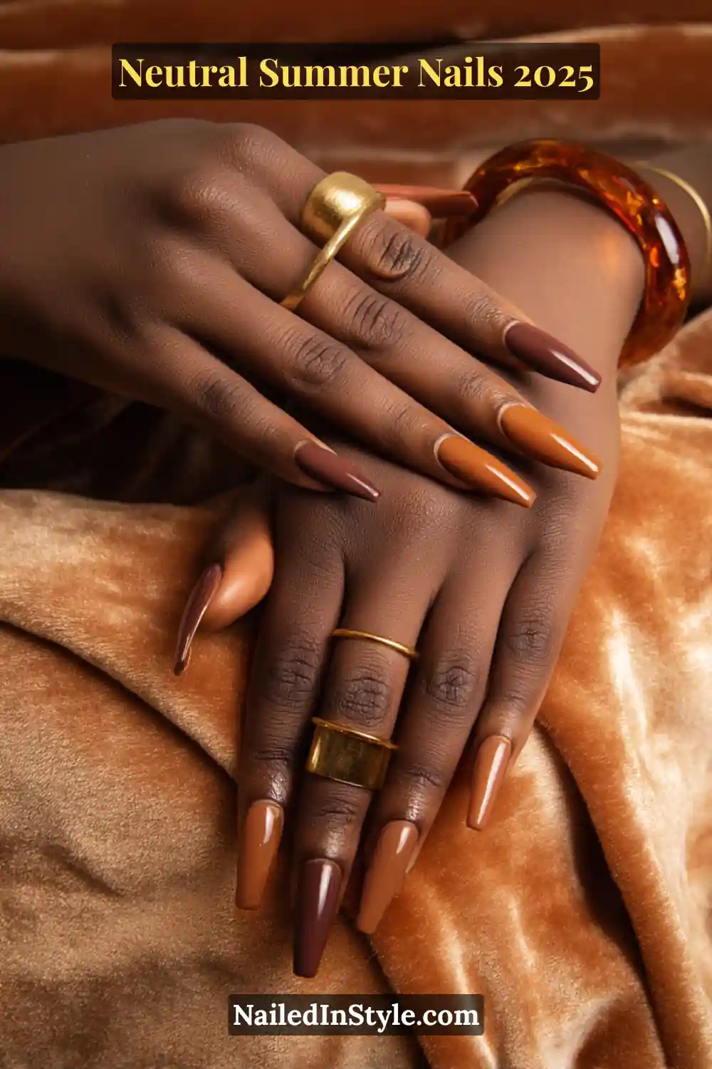 Neutral Summer Nails 2026: Clean, Chic & Warm-Weather Ready 5 Close-up of hands with deep skin tone showcasing long coffin-shaped nails in glossy espresso, rich bronze nude, and warm amber hues, paired with gold statement rings and velvet background.