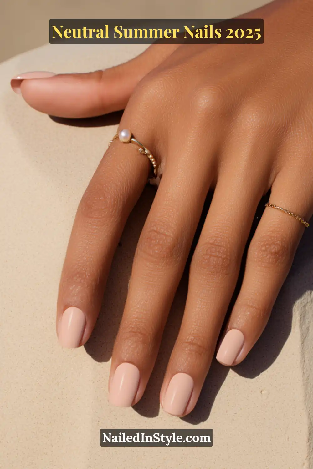 Neutral Summer Nails 2026: Clean, Chic & Warm-Weather Ready 15 Close-up of a medium-toned hand with short natural nails painted in sand beige polish, accessorized with delicate gold and pearl rings.