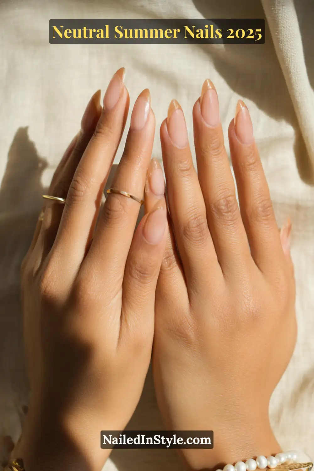 Neutral Summer Nails 2026: Clean, Chic & Warm-Weather Ready 22 Two hands with almond-shaped nude nails featuring delicate tan French tips, accessorized with minimal gold rings and a pearl bracelet on medium skin.