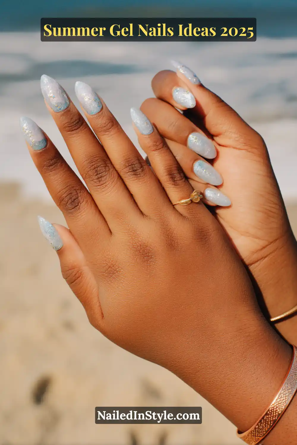 Summer Gel Nails Ideas 2026 13 Close-up of hands with almond-shaped gel nails in an ice blue aura design, enhanced with shimmering silver foil accents, captured at the beach.