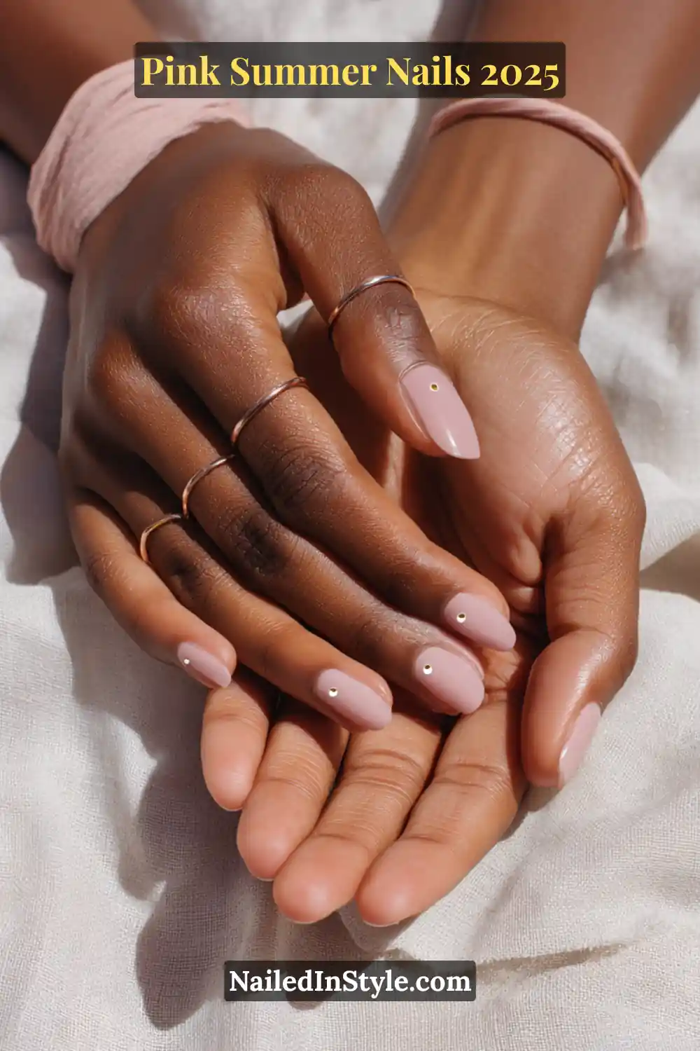 Hands with soft pastel pink nails, each featuring a tiny gold dot accent in the center, styled with delicate rings.