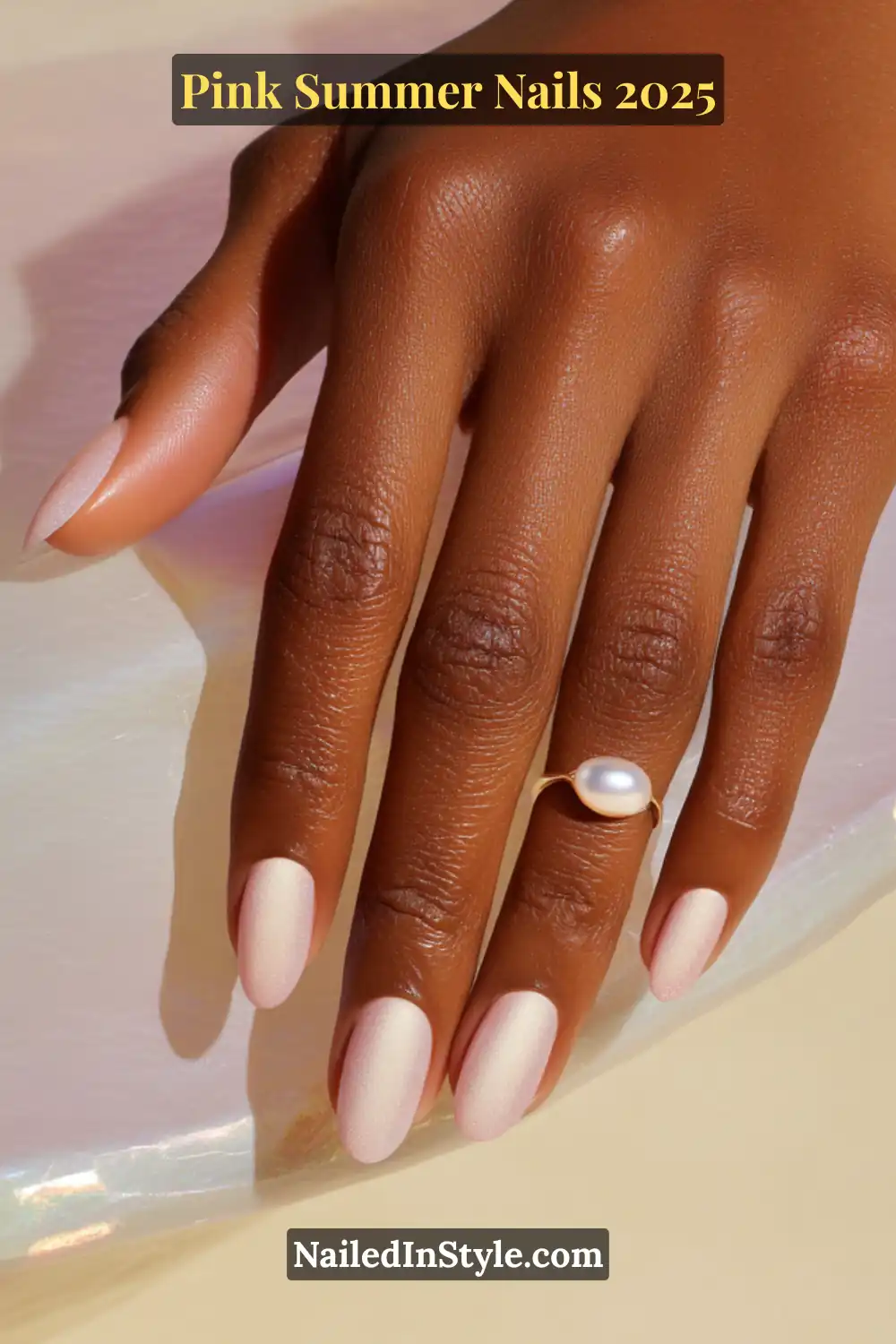 Close-up of a hand with almond-shaped pearl pink gradient nails and a gold ring with a white pearl.