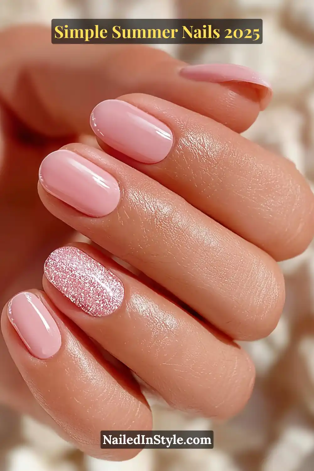 A close-up of a hand with warm-toned skin showcasing short rounded nails painted in soft baby pink, with the ring finger featuring a sparkling pink glitter accent.